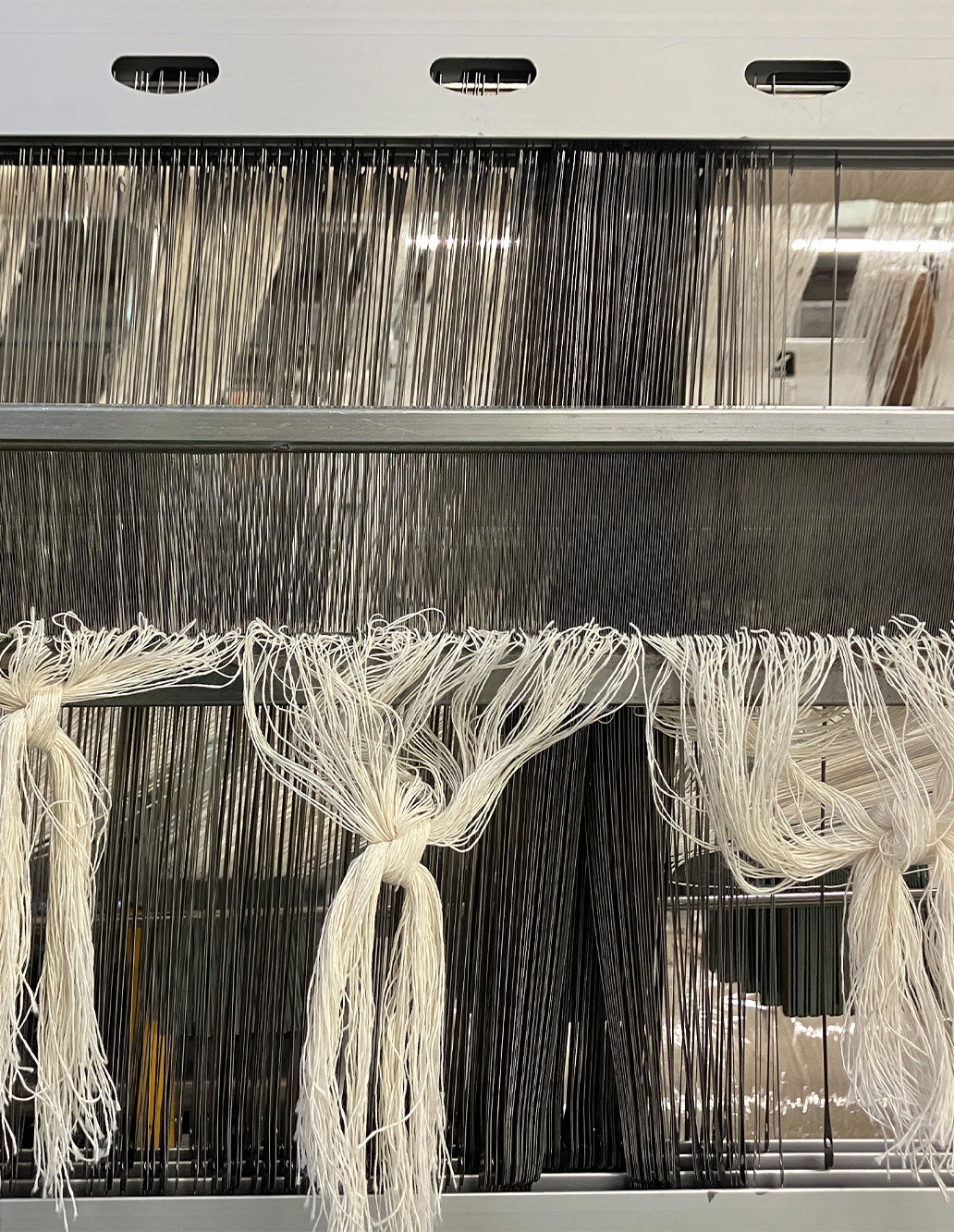 Undyed linen threads hanging through weaving machinery