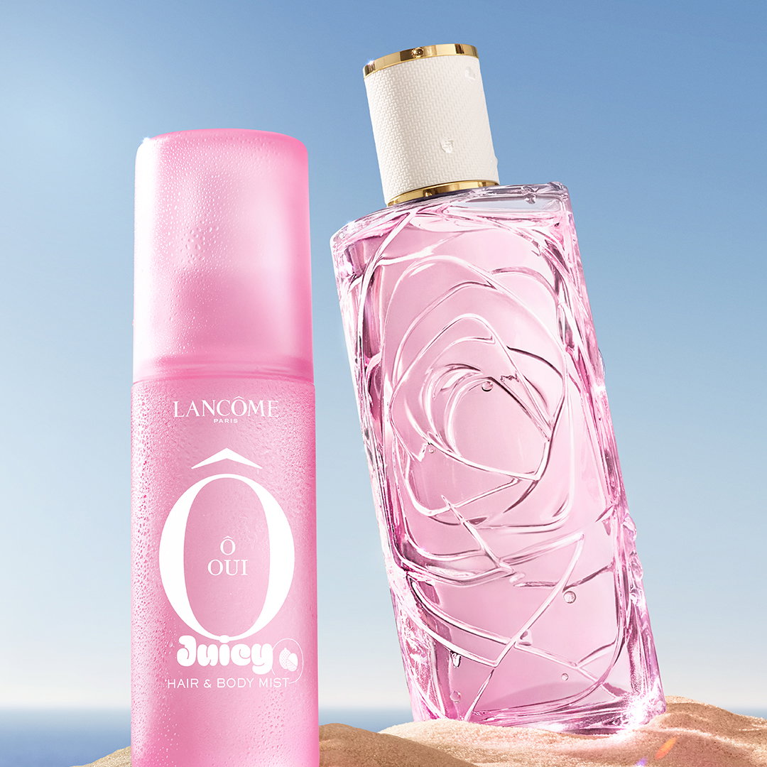 La nuova mist Ô Oui e l'iconico profumo Ô de Lancôme, entrambi rosa, affiancati su una spiaggia sabbiosa.