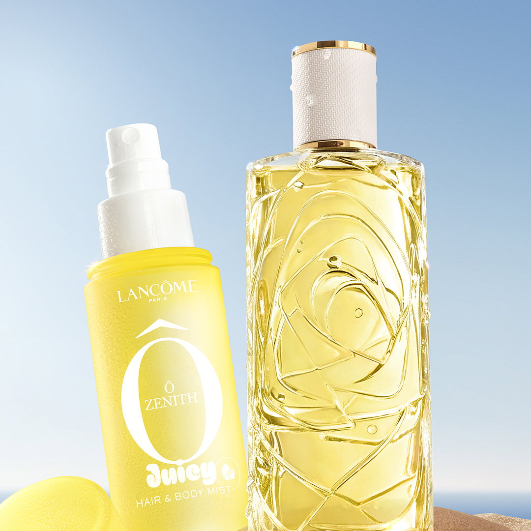 La nuova mist Ô Zenith e l'iconico profumo Ô de Lancôme, entrambi gialli, affiancati su una spiaggia sabbiosa.