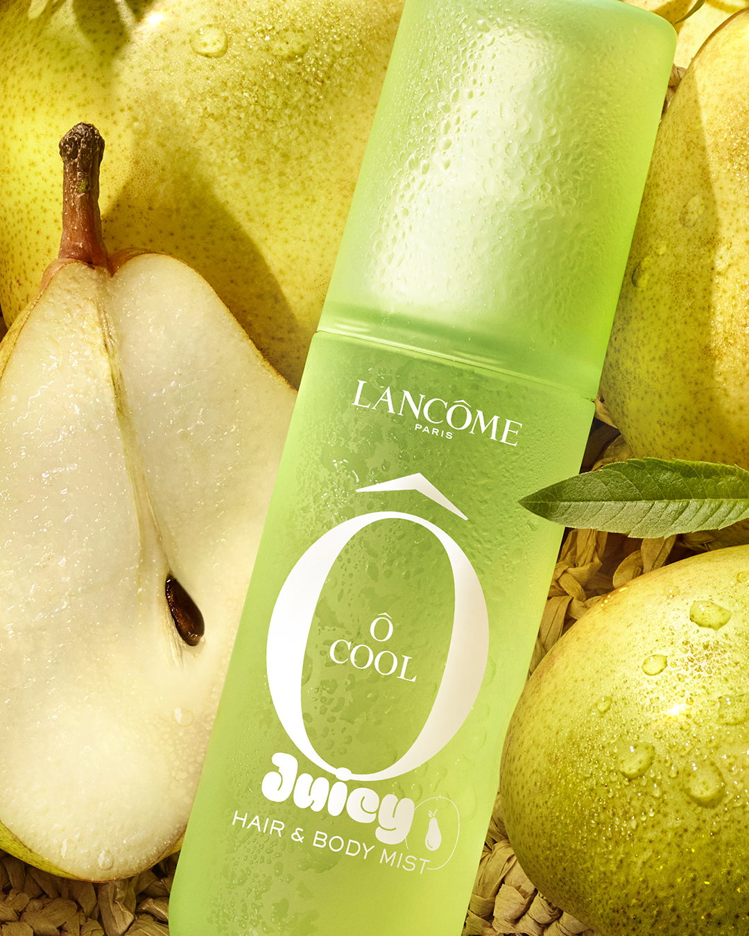 Lancôme Ô Cool Hair & Body Mist. Flacone verde satinato tra pere fresche e bagnate di rugiada, evocando freschezza.