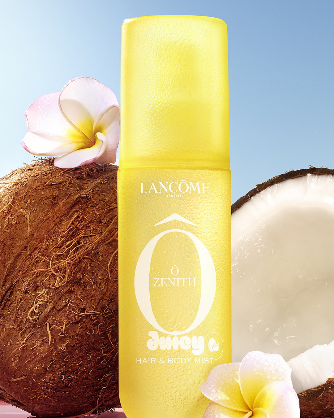 Lancôme Ô Zenith Hair & Body Mist. Flacone giallo solare con cocco e fiori di frangipane su uno sfondo di cielo azzurro.
