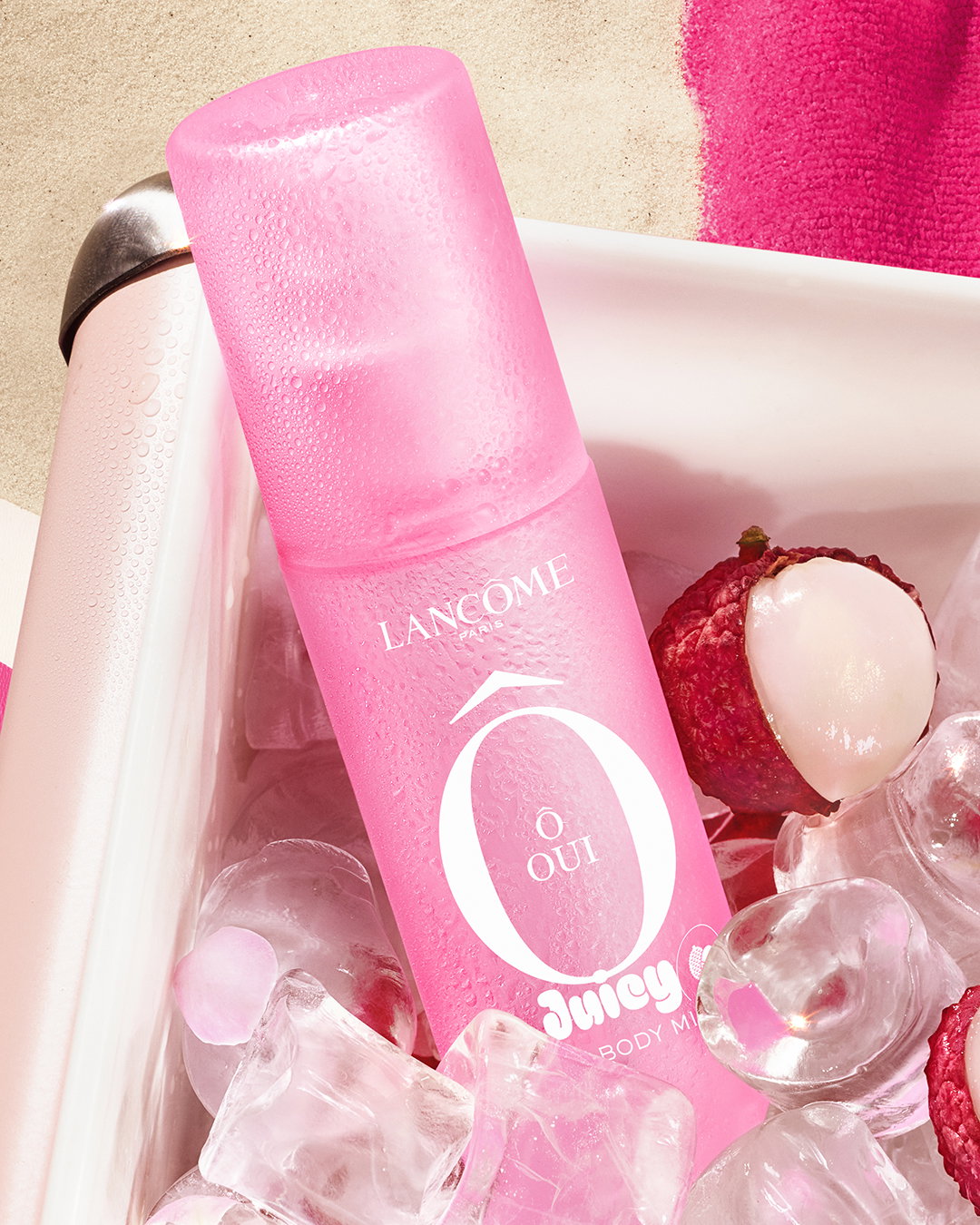 Lancôme Ô Oui Hair & Body Mist. Flacone rosa immerso in un contenitore con ghiaccio e litchi freschi, per un look estivo.