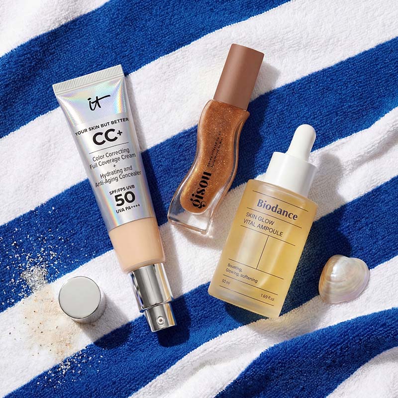 Skincare products on a blue and white striped towel, including a CC cream, glow serum, ampoule, and an open compact with a pearl.