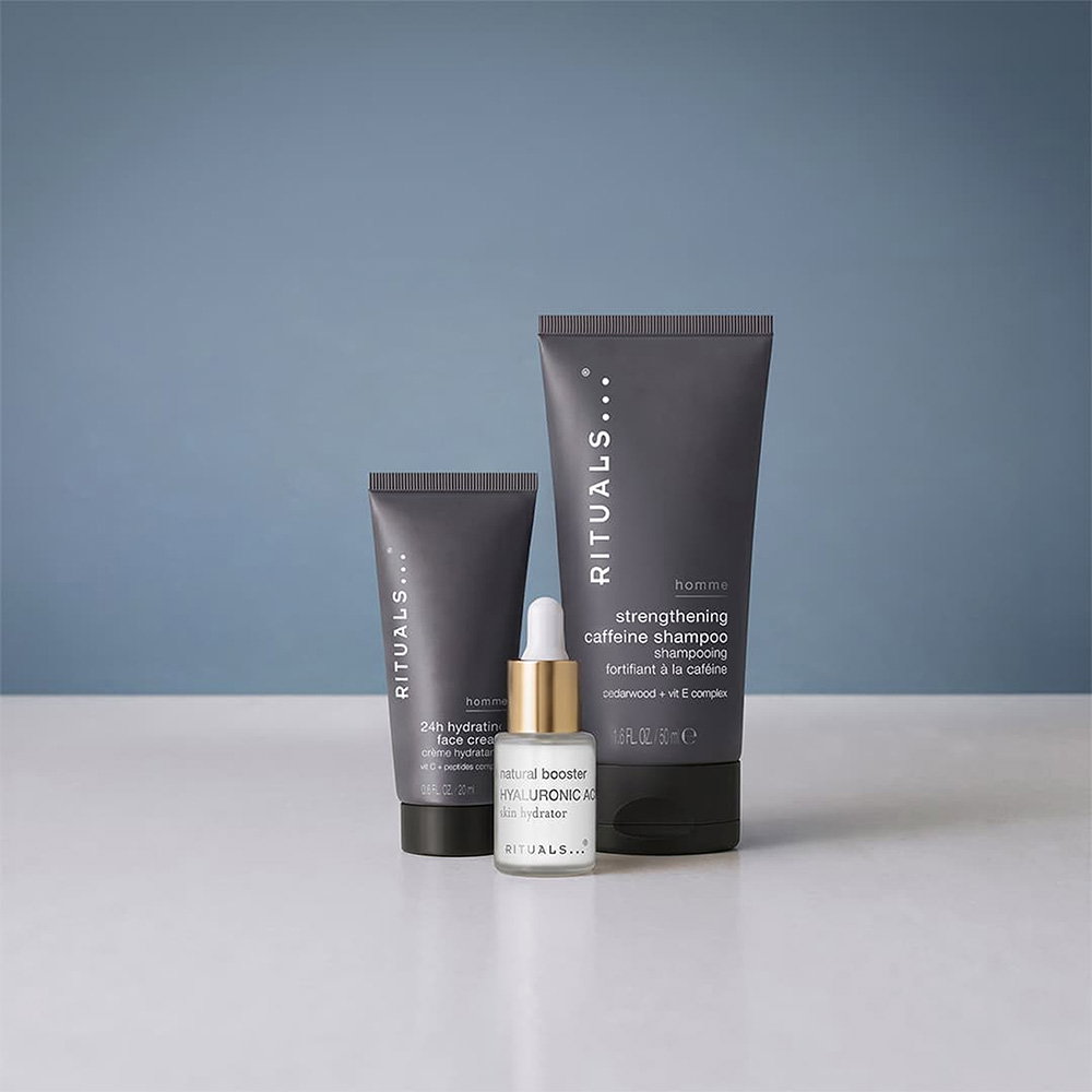 Three Rituals brand grooming products, including a shampoo and serum, against a blue background.