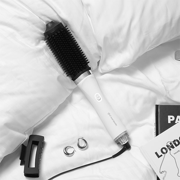 A hair styling tool, magazine, hair clip, and earrings on a white bed.