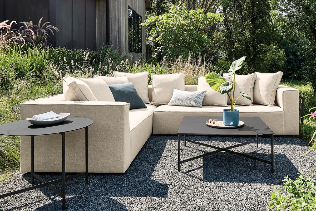 Oasis sectional with cream cushions and accent pillows around black tables in a landscaped outdoor setting.