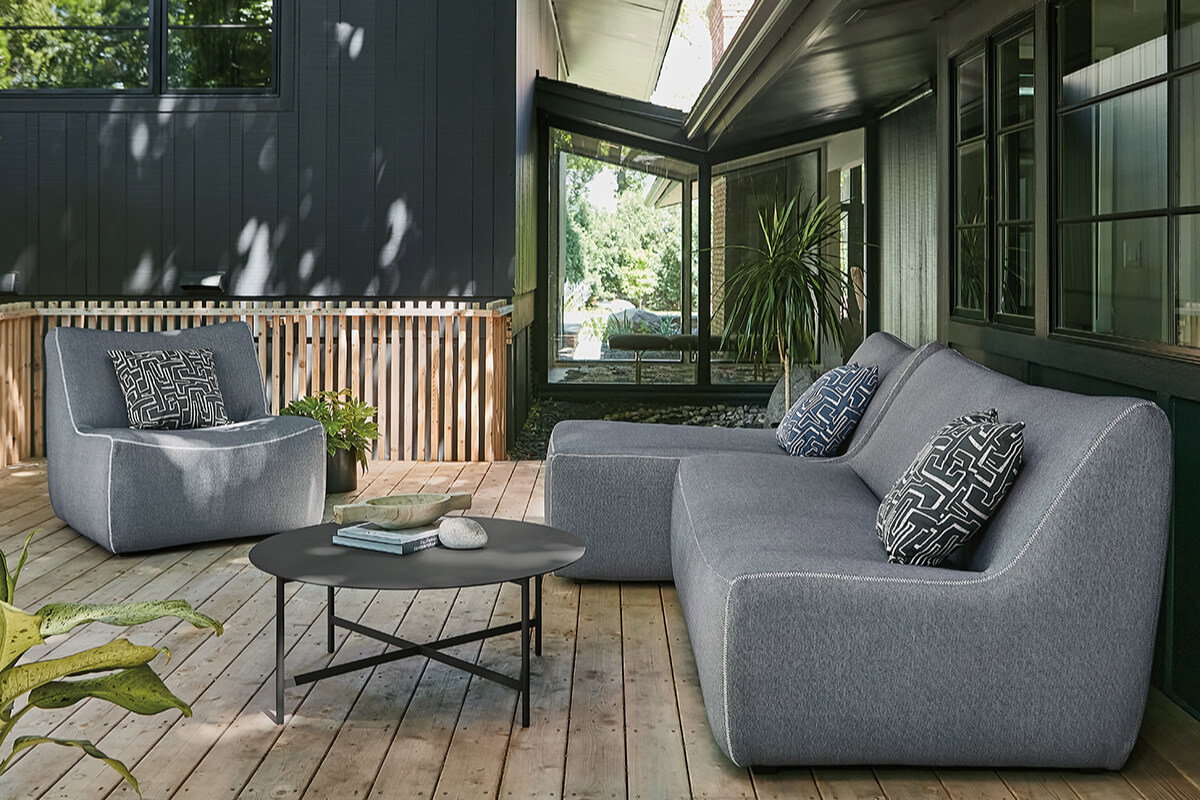 Grey Maya sofa with chaise and Circuit coffee table on a wood deck beside a modern home.