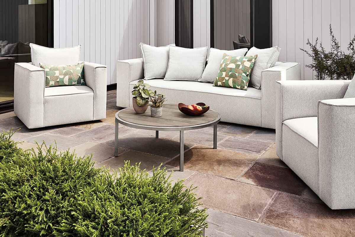 Oasis outdoor sofa and chairs with white cushions gathered around a round Montego coffee table on a stone patio.
