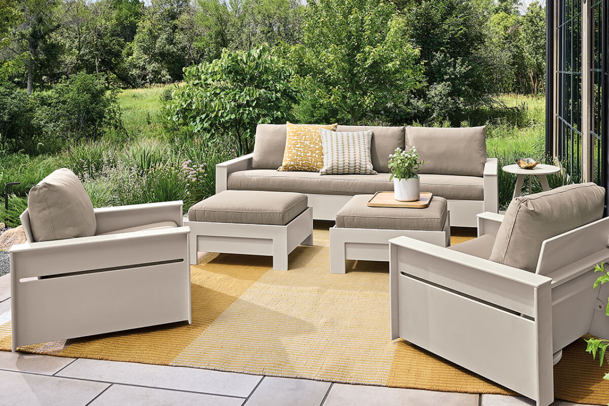 Outdoor seating area with Rayo sofa, chairs and ottomans overlooking a landscaped garden.