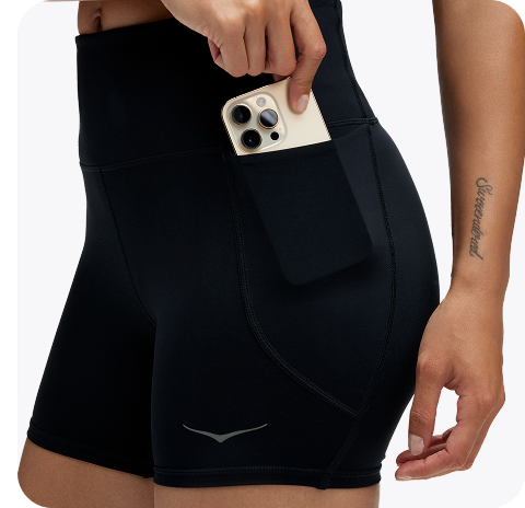 An image of a person from the back wearing the Hupana Sports Bra, a trail run hat, a close up of a person zipping up the Skyflow Jacket, and a close up of a person wearing the Elaro Biker shorts placing a phone into the side pocket.