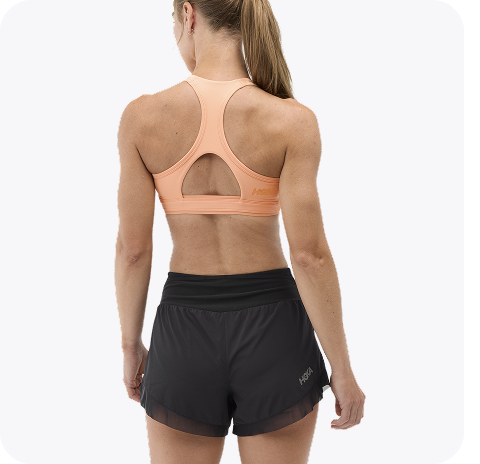 An image of a person from the back wearing the Hupana Sports Bra, a trail run hat, a close up of a person zipping up the Skyflow Jacket, and a close up of a person wearing the Elaro Biker shorts placing a phone into the side pocket.