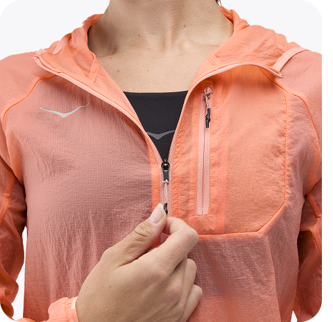 An image of a person from the back wearing the Hupana Sports Bra, a trail run hat, a close up of a person zipping up the Skyflow Jacket, and a close up of a person wearing the Elaro Biker shorts placing a phone into the side pocket.