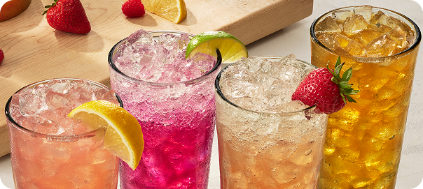 Assorted iced drinks in glasses garnished with lemon, lime, and strawberries.