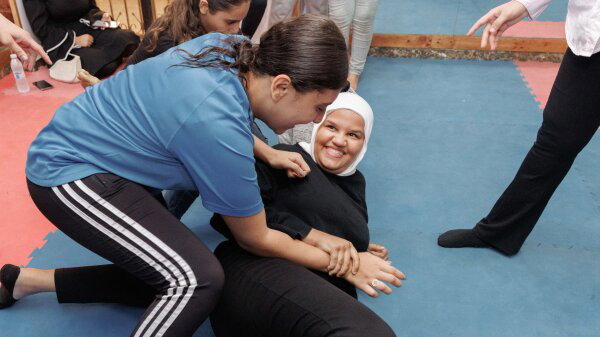 Palestinian girls train in jiu jitsu in the refugee camp of Bourj el Barajneh in South Beirut. One girl lying on the ground smiles up at another girl on top of her. 