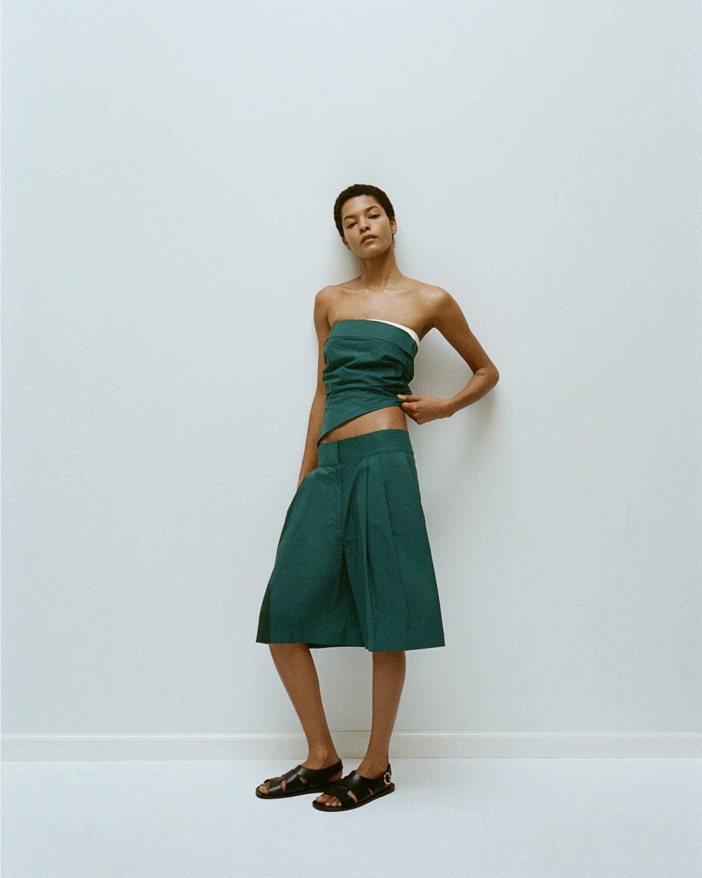 Model standing against white background wearing Maisy Strapless Top in Poplin in spruce with Clio Short in Poplin in spruce, with Capri Fisherman Sandals in black