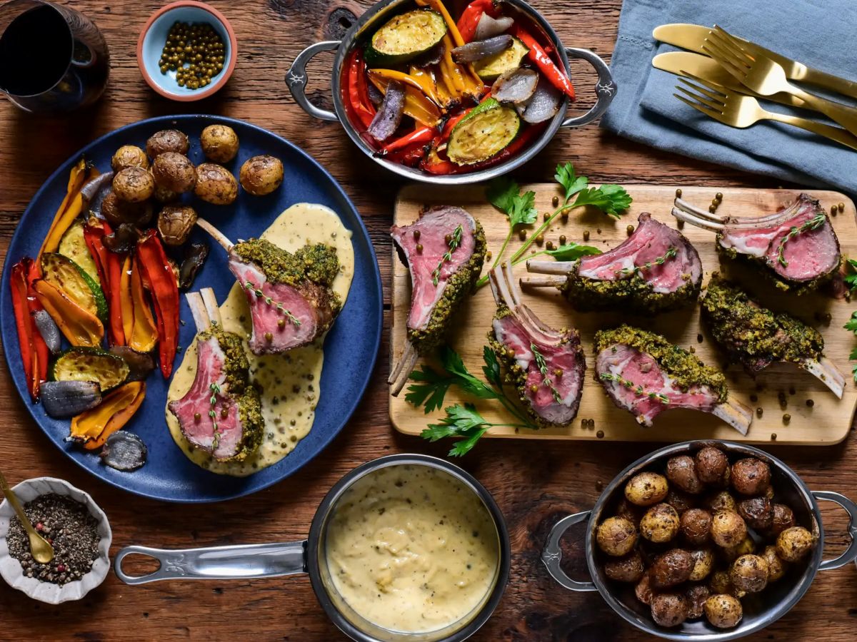 IMG: Herb-Crusted Rack of Lamb on wooden table, with various side dishes