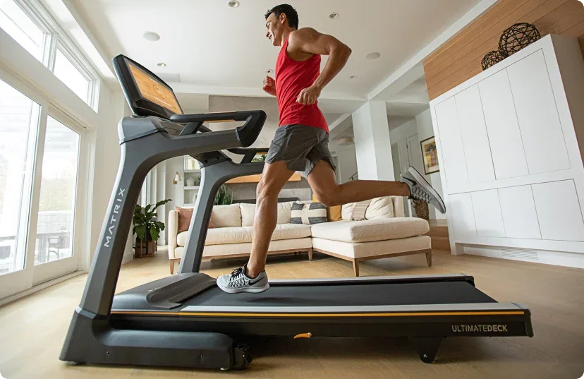 Man in red tanktop and grey shorts running on Matrix treadmill in home