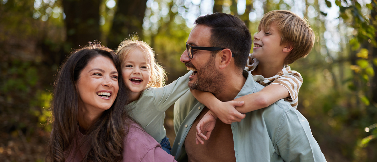 Fröhliche Familie mit zwei Kindern im Wald. Eltern und Kinder lachen und umarmen sich beim gemeinsamen Spaziergang im Freien.