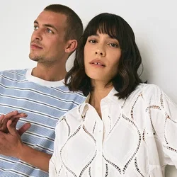T-shirt rayé bleu et blanc associé à un pantalon beige, à côté d'une chemise en dentelle blanche avec des découpes en losange et un pantalon rayé. Fond uni.