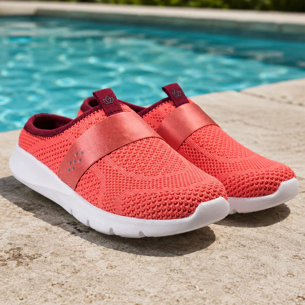 Coral mesh slip-on sneakers with white soles displayed poolside on concrete decking.