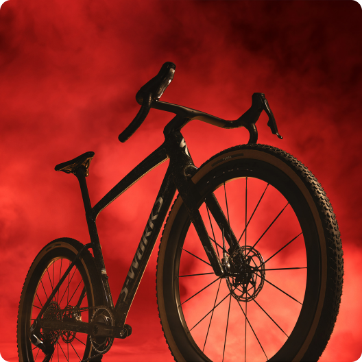 Black gravel bike silhouette with drop handlebars and disc brakes against a dramatic red smoky background