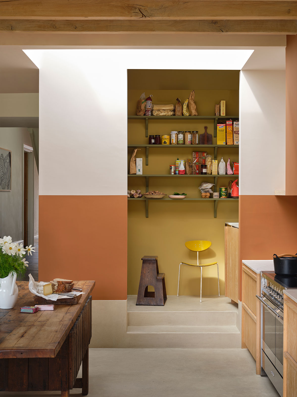 We’re drawn immediately into the small nook of a pantry in this kitchen. The outside wall is split between a bright white and warm terracotta colour, while the pantry wall is a complete contrast with a luscious citrus tone on the wall and ceiling, with green shelves. It’s such a colourful space with all the packets and jars, as well as the vivid yellow chair.