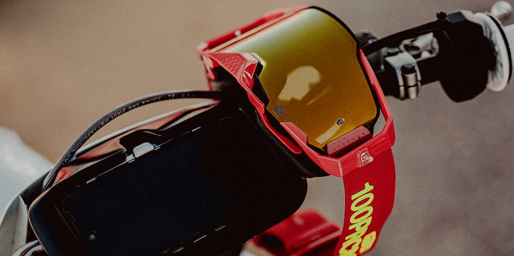 Close-up of red 100% Armega goggles mounted on a motocross bike