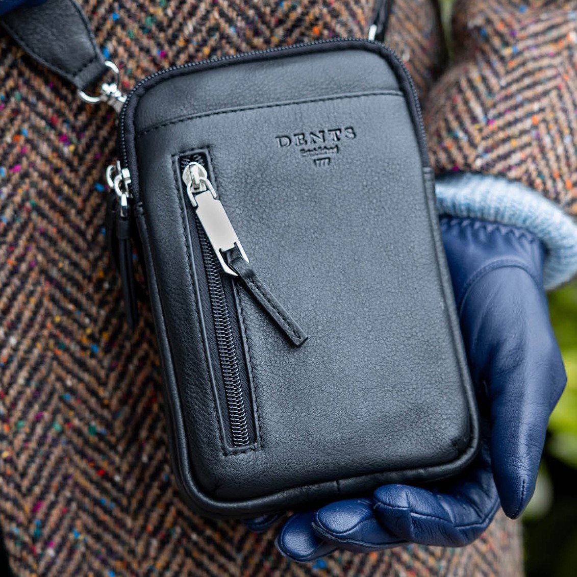 Close up of a man holding a black crossbody phone bag 