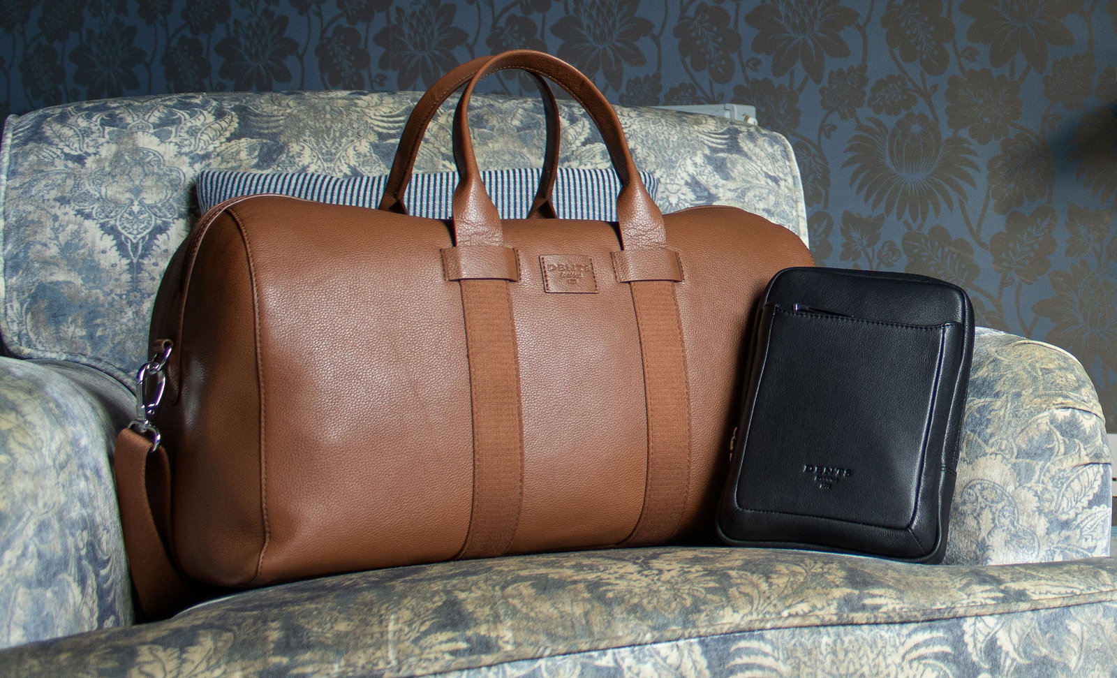 Men's weekend bag and small crossbody bag laid out on a sofa