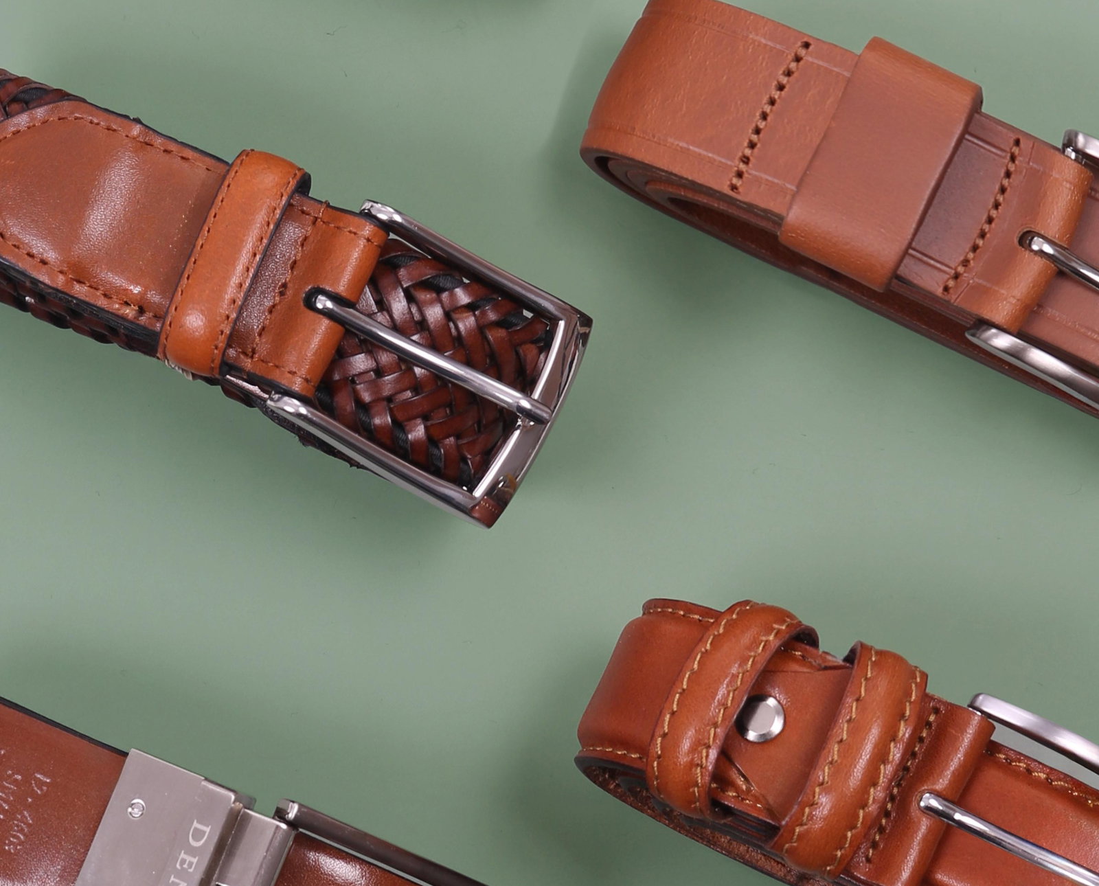 Variety of men's leather belts in various styles and colours on a green background