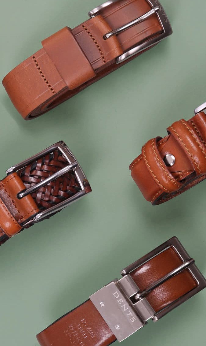 Variety of men's leather belts in various styles and colours on a green background