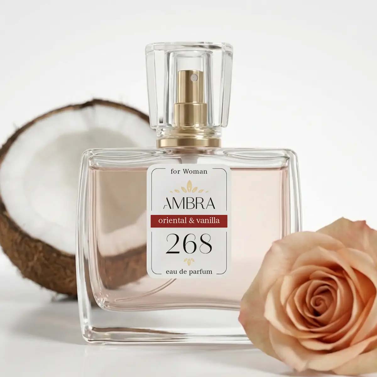 Glass perfume bottle labelled 'AMBRA 268' (oriental & vanilla) with coconut half and peach rose on white background
