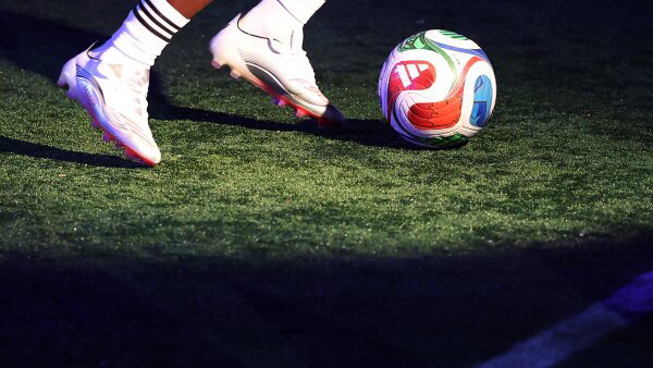 A close-up shot of a person’s feet in cleats running with a soccer ball on grass. 