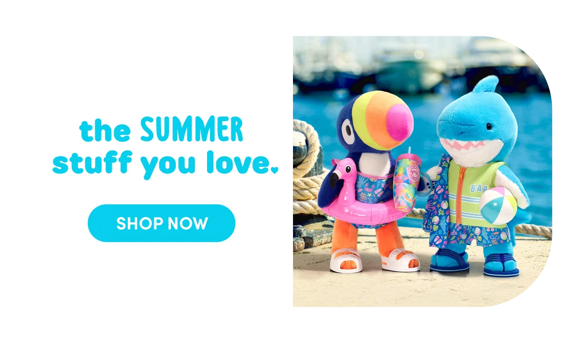 Two plush characters stand side by side at a dockside setting with water and boats in the background. One is a toucan plush wearing a pink inflatable swim ring, a bathing suit, and white sandals, holding a colorful drink. Next to it is a blue shark plush wearing a green life vest with BAB lettering, patterned swim shorts, and holding a beach ball. On the left, teal text reads the SUMMER stuff you love. A rounded teal button below reads SHOP NOW.