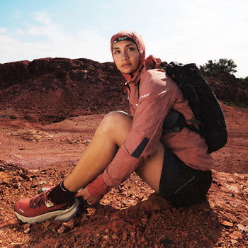 Hiker in red jacket and backpack resting on red rocky terrain under a blue sky