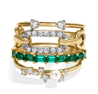 Stacked yellow gold rings with emerald gemstones, diamonds, and pearl accents.
