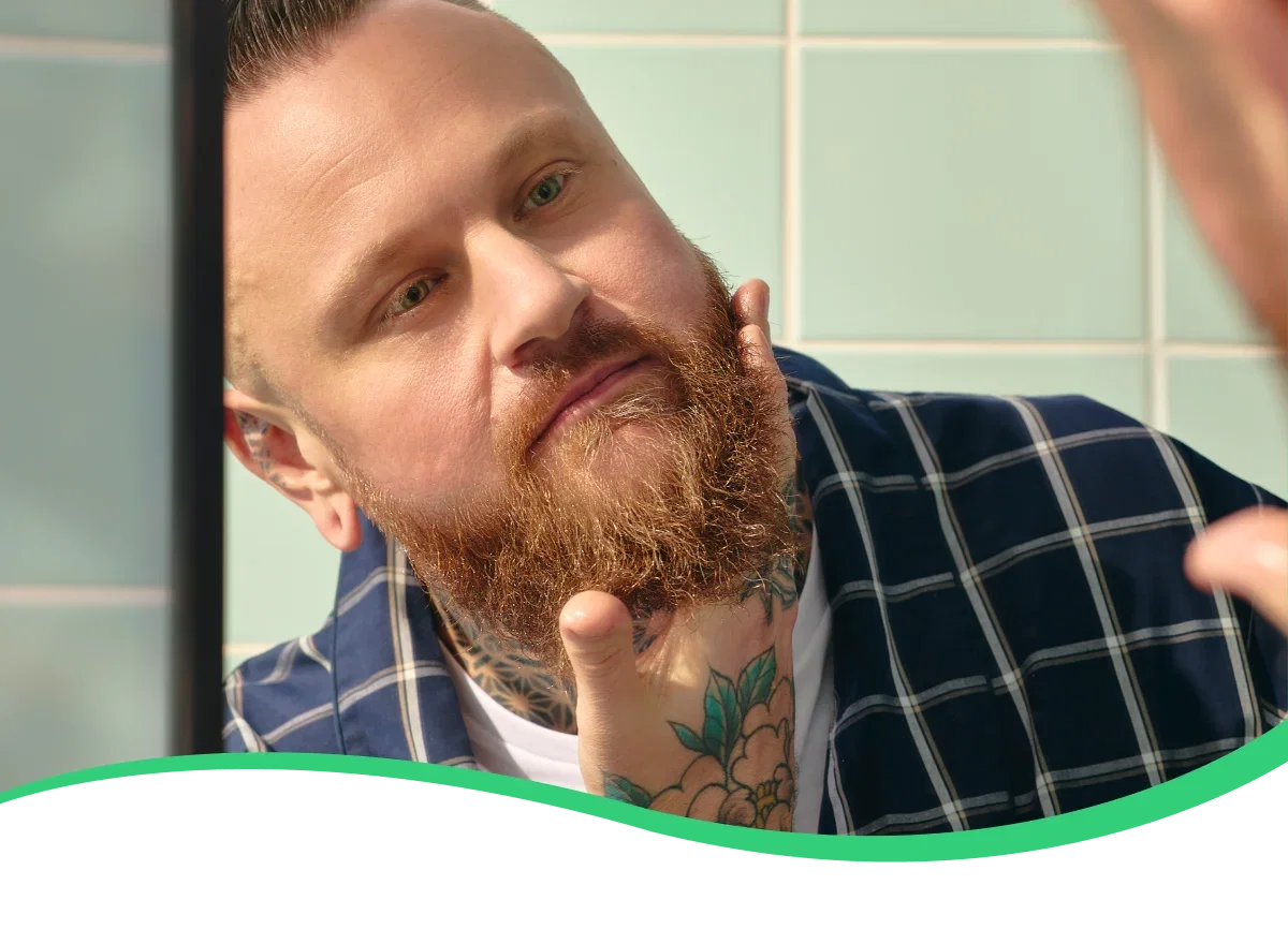 Hero image: A person applying oil to their beard in the mirror