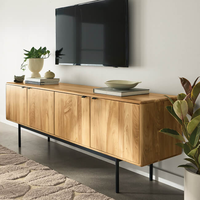 Hensley wood media console with black legs beneath a wall-mounted TV and decorative accents.