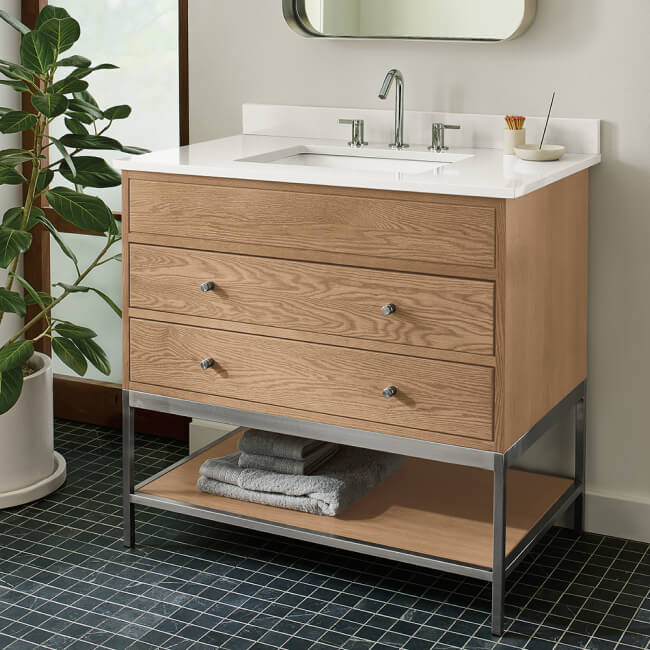Linear bathroom vanity in light wood with white countertop, drawers and lower shelf storage.