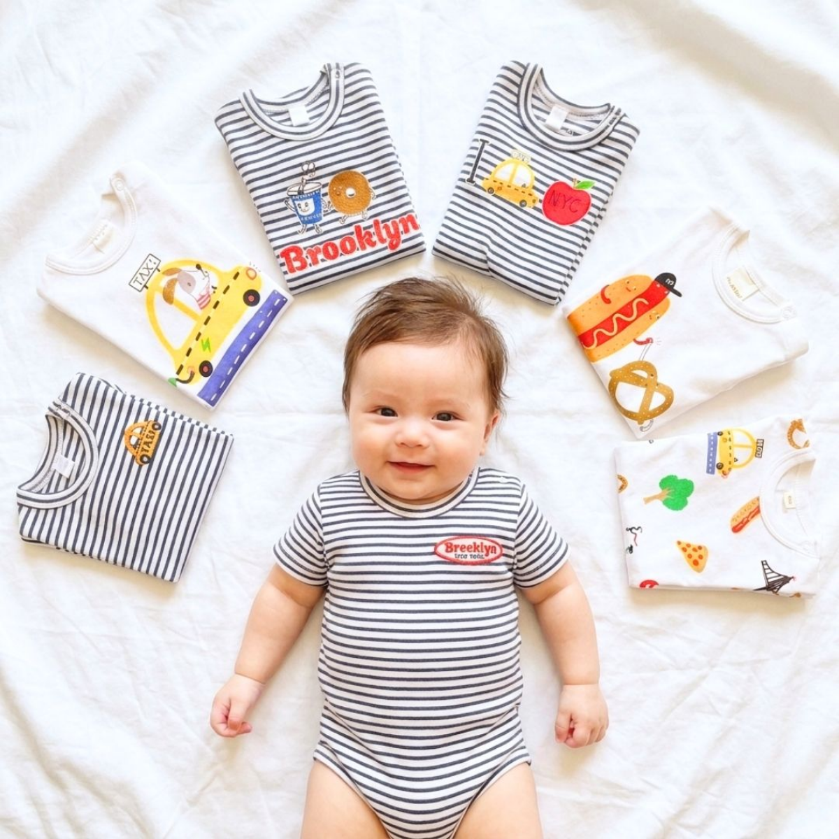 Smiling baby surrounded by 7 Days in NYC Bodysuits — a full week of New York love