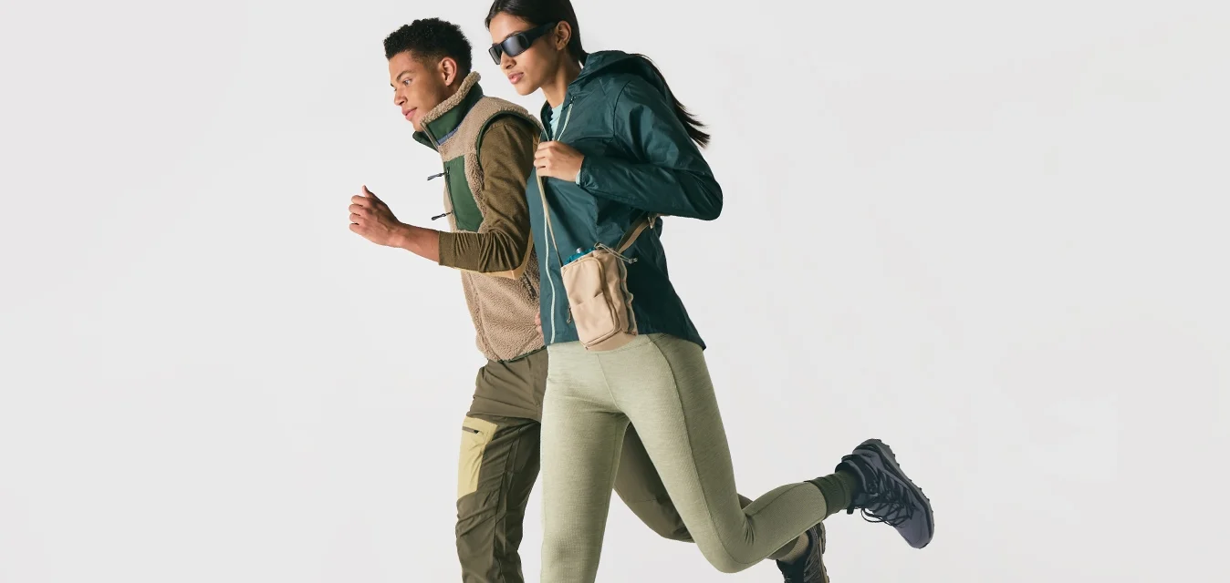 Twee personen gekleed in sportieve buitenkleding en sneakers, die zij aan zij rennen tegen een effen witte achtergrond.
