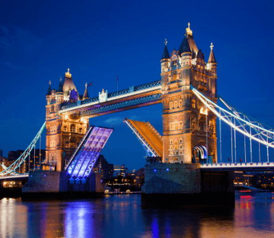 Tower Bridge illuminated at night with one side raised, reflecting in the water below.