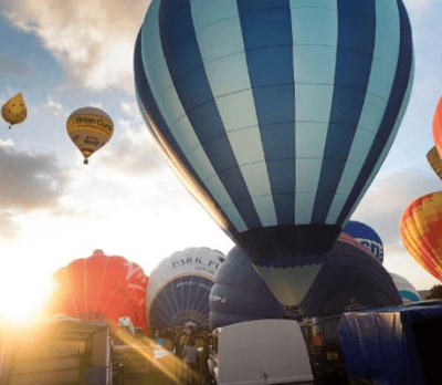 Hot air balloons in various colours at sunrise, with one balloon ascending in the background.