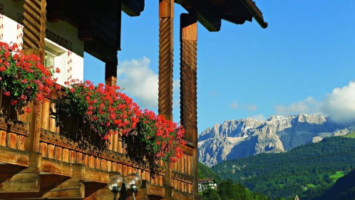 Uriges Hotel mit Holzfassade mit roten Blumen am Balkon und traumhaftem Bergblick