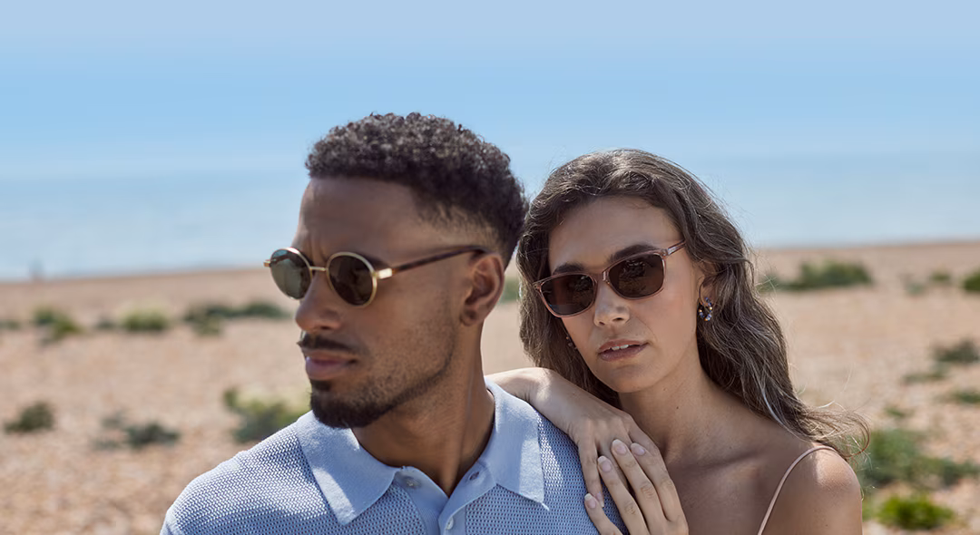 Man in round sunglasses and woman in cat-eye sunglasses, on a beach