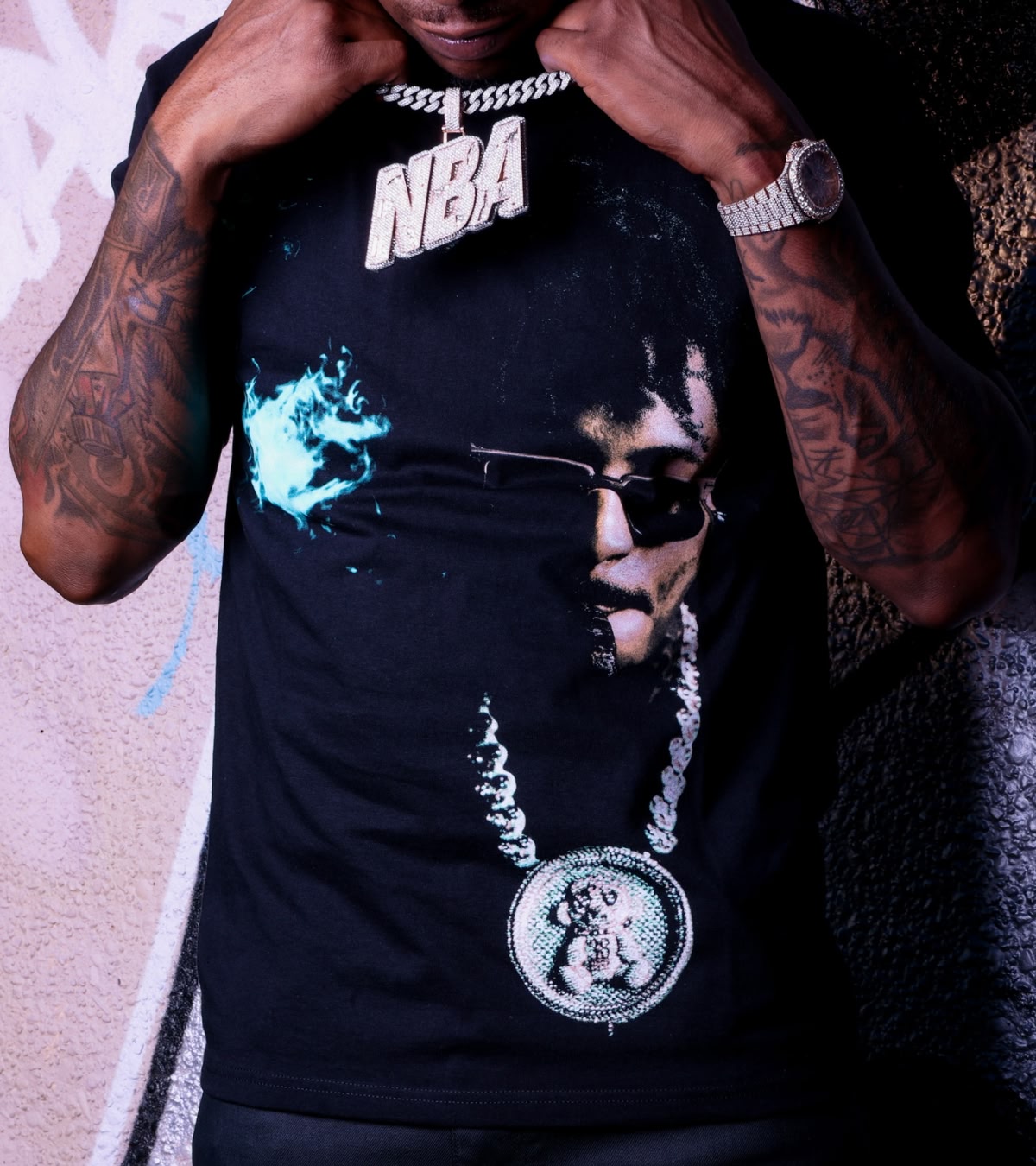 Shop NBA YoungBoy | The rapper holding onto a chain that has an "NBA" chain, wearing a shirt that also showcases the chain.