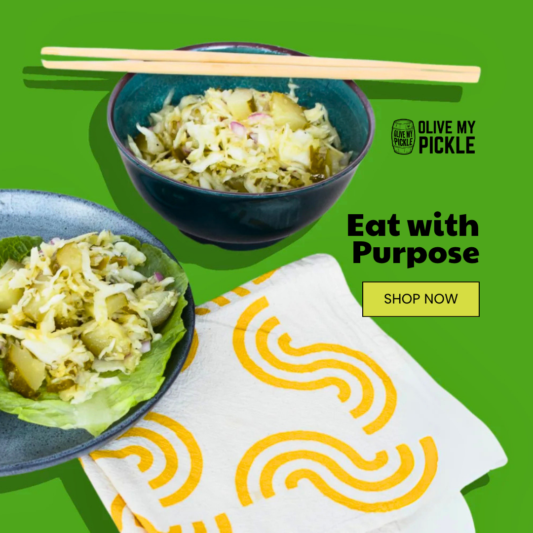 Two bowls of chopped pickle and cabbage salad, one with chopsticks, on a green background. A patterned napkin, 'Olive My Pickle' logo, and 'Eat with Purpose' te