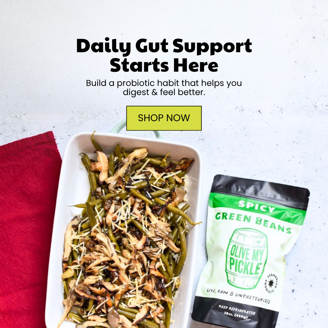 Prepared dish of green beans with mushrooms and cheese next to a black and green pouch of Olive My Pickle Spicy Green Beans, on a speckled grey surface with a r