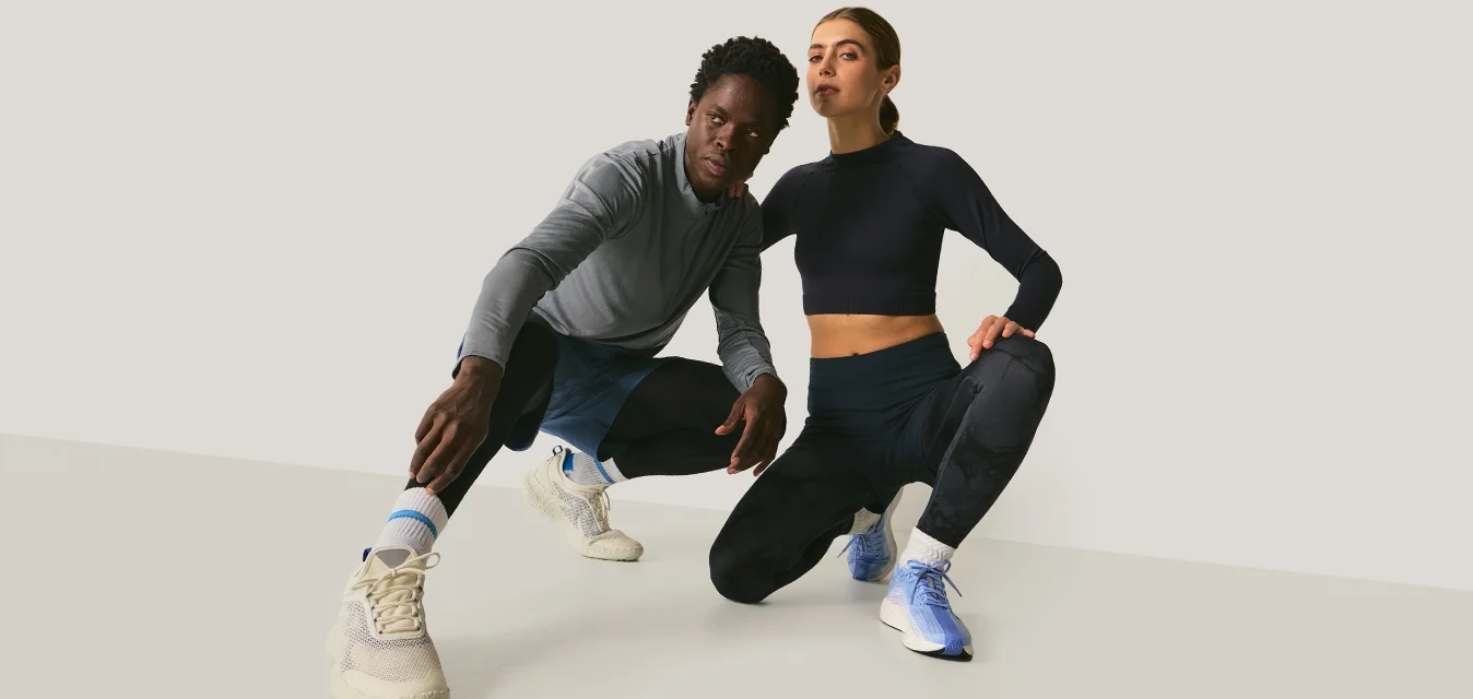 Deux athlètes en tenue de sport sont accroupis côte à côte sur un fond uni, posant avec assurance et des expressions concentrées.