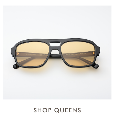 A studio product shot of the Queens sunglasses, featuring a black acetate square-shaped aviator frame with a double bridge and amber-yellow tinted lenses. Simple text below reads, 